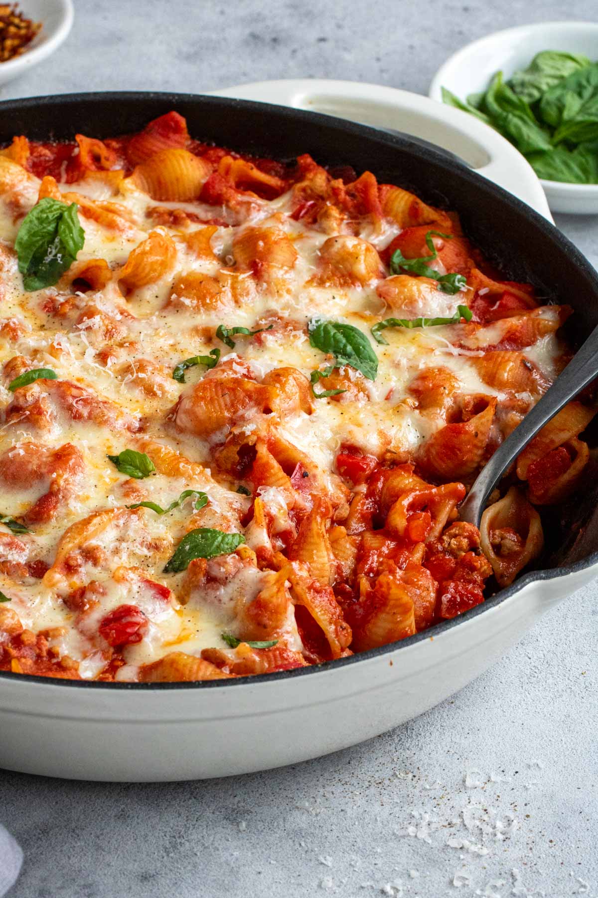 Close up of a serving ground turkey pasta bake casserole with parmesan and a spoon and basil in the background.