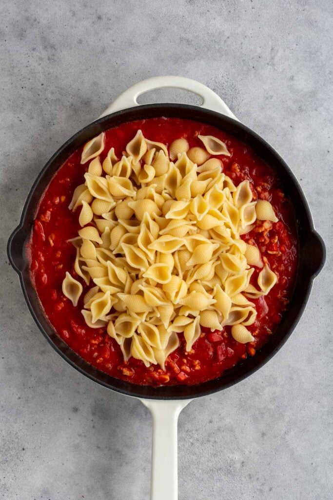 Cast iron skillet with cooked ground turkey, sautéed veggies, tomato sauce, and cooked pasta on top.