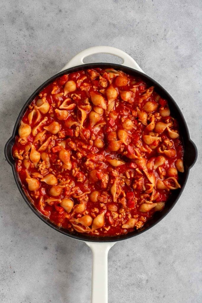 Cast iron skillet with cooked ground turkey tomato sauce with cooked pasta shells.