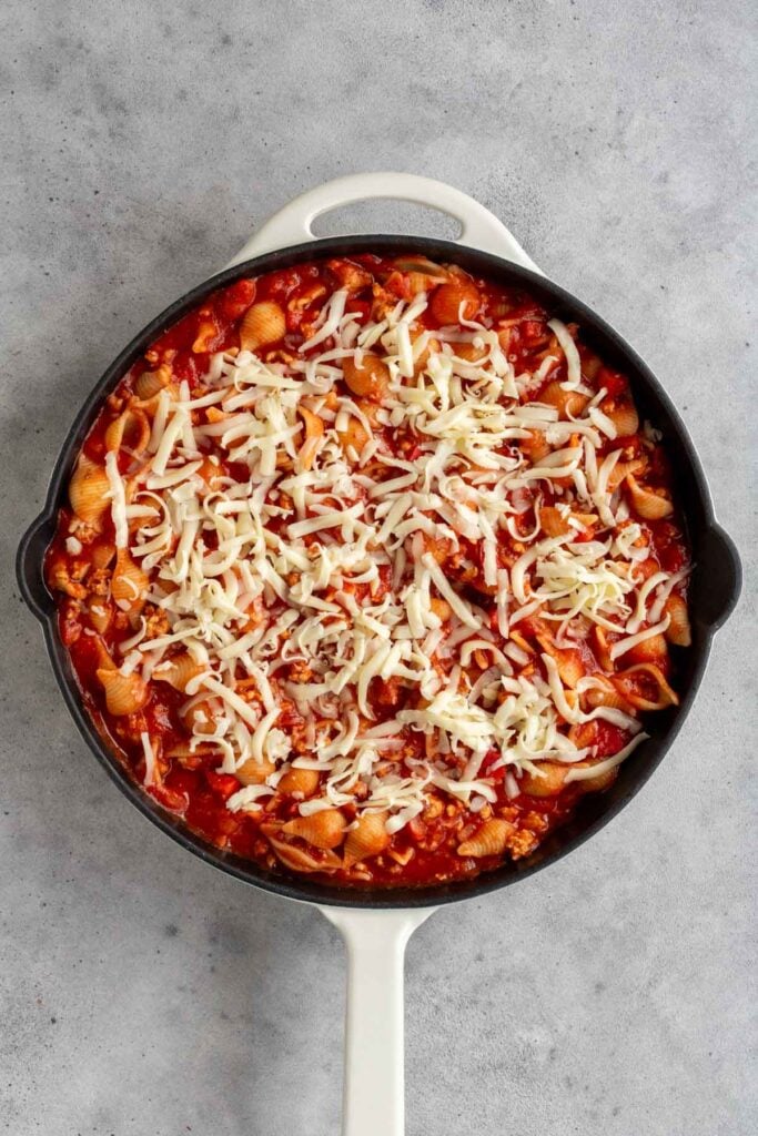 Cast iron skillet with cooked ground turkey tomato pasta with shredded mozzarella cheese on top.