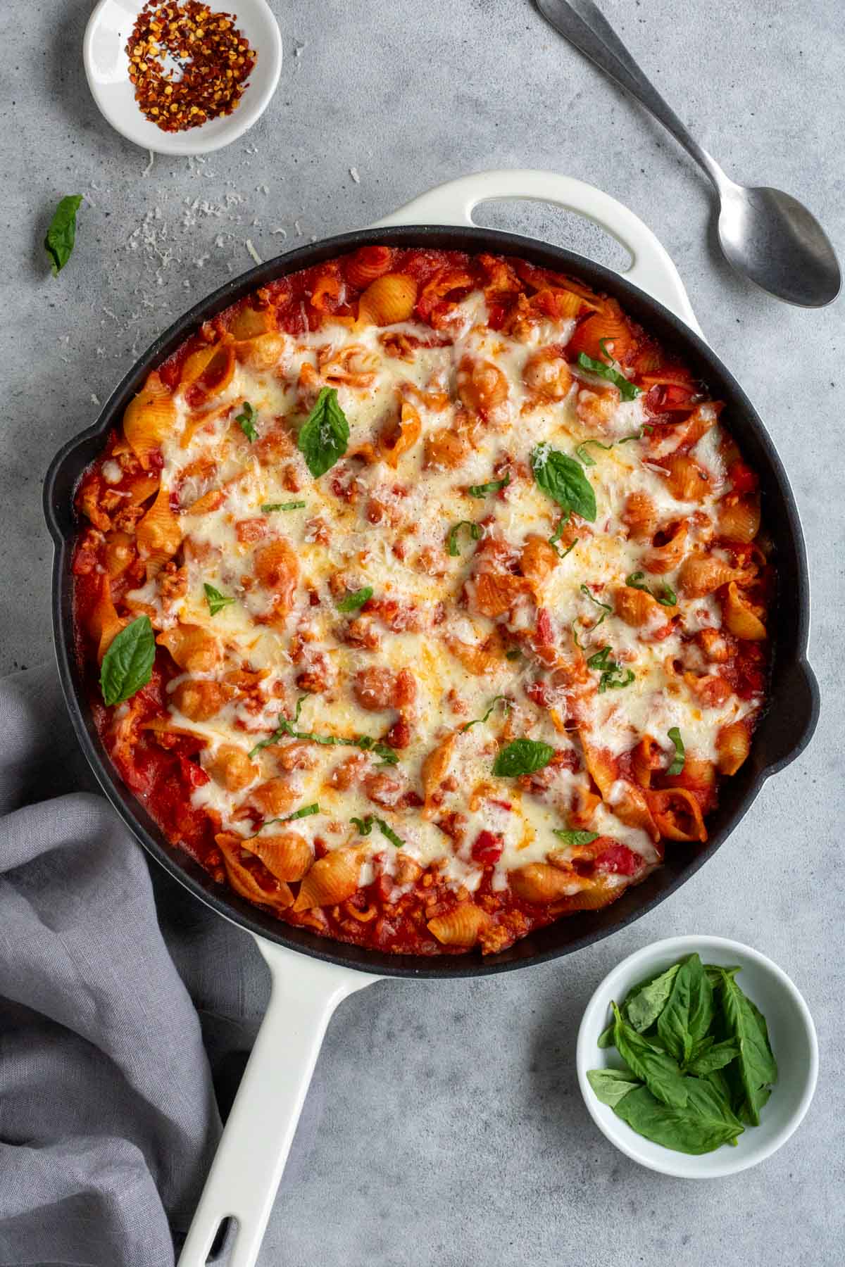 Cast iron skillet with cooked creamy ground turkey pasta bake with fresh basil and grated parmesan cheese on top.