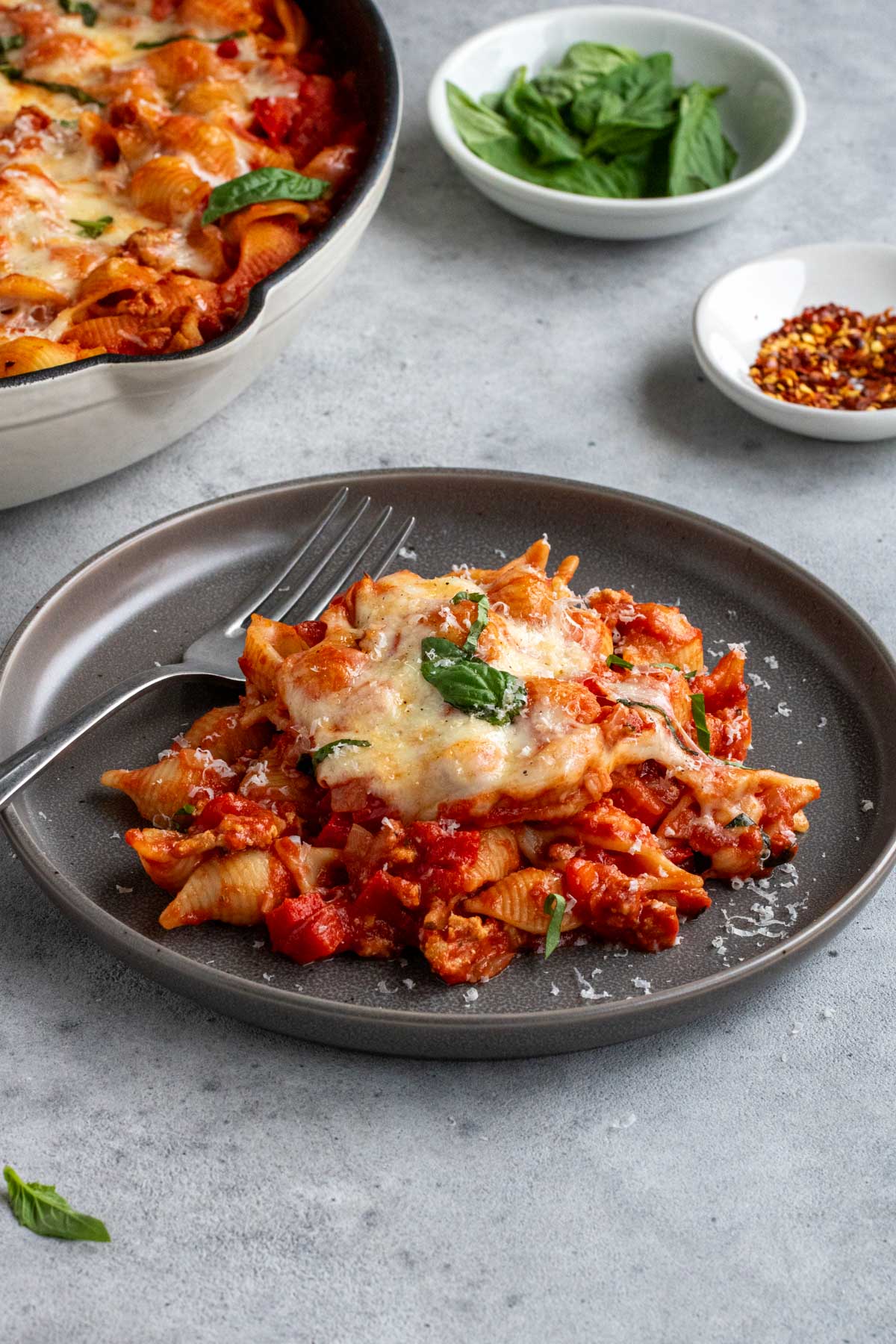 Serving of ground turkey pasta bake on a plate with a side of bread and parmesan cheese on top.