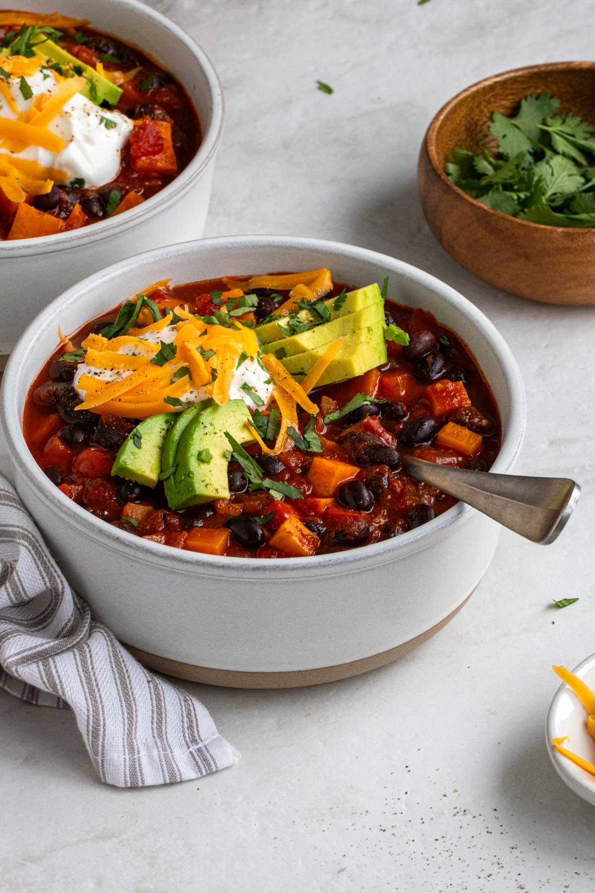 Close up of a bowl of sweet potato black bean chili with sour cream, cheddar cheese, avocado, and fresh cilantro on top.