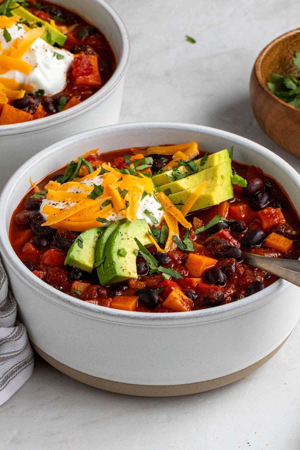 Two bowls of sweet potato black bean chili with a side or tortilla chips and fresh cilantro.