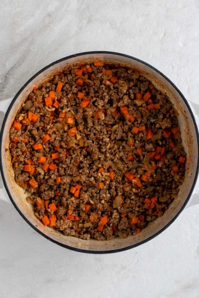 Large pot with cooked ground meat, sautéed onion, carrots, garlic, paprika, salt, and pepper. 