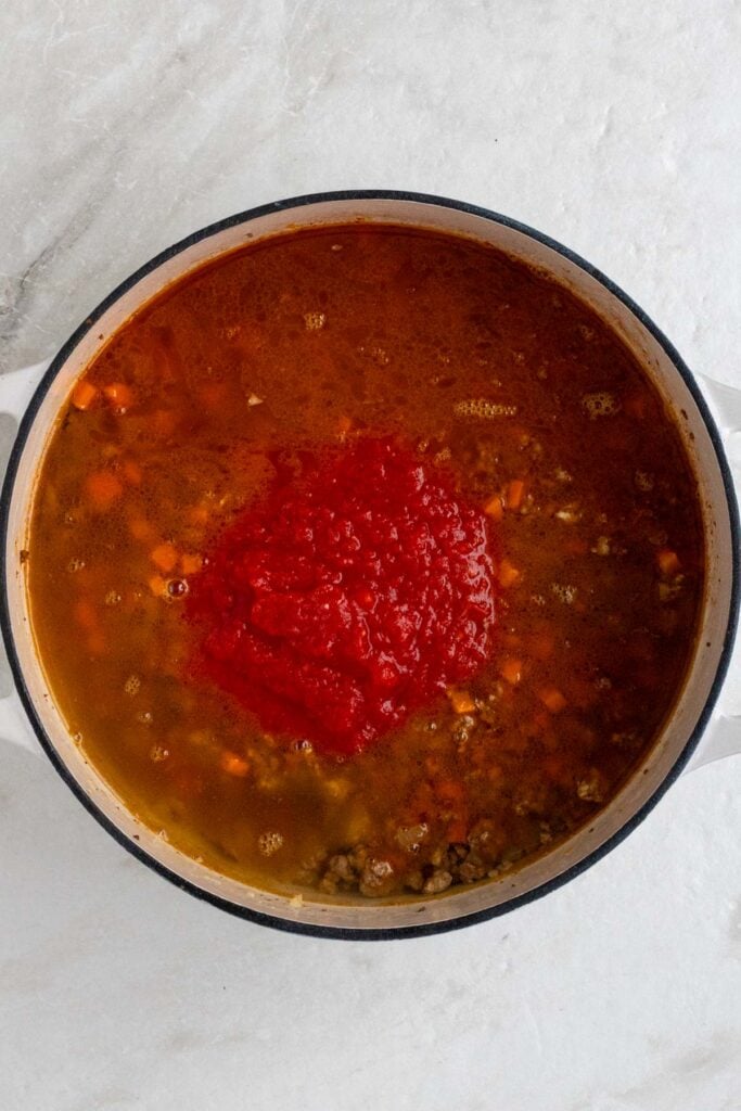 Large pot with cooked ground meat, sautéed vegetables, spices, tomatoes, and beef broth.