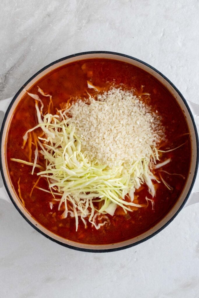 Large pot with ground meat, vegetables, spices, tomatoes, beef broth, uncooked rice, and chopped cabbage.