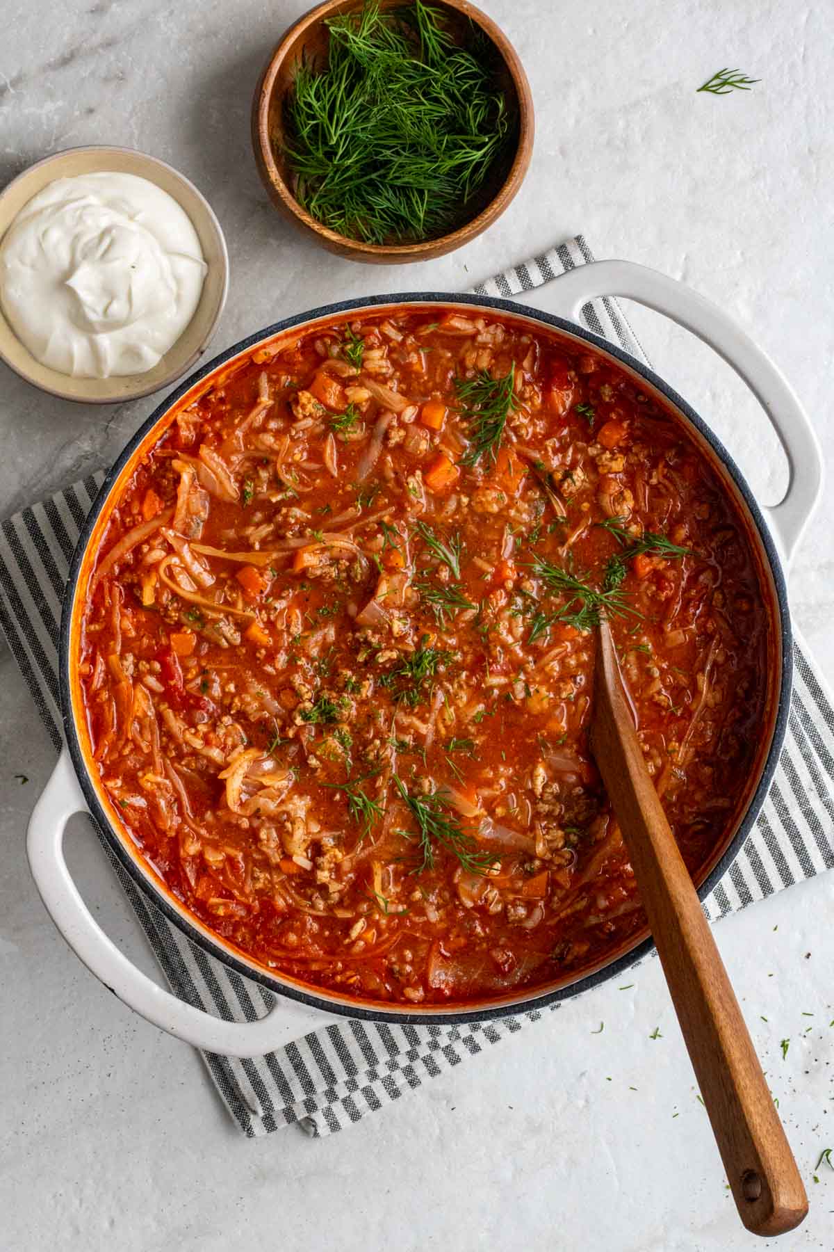 Large pot with unstuffed cabbage roll soup with a serving spoon with fresh dill and sour cream on the side.