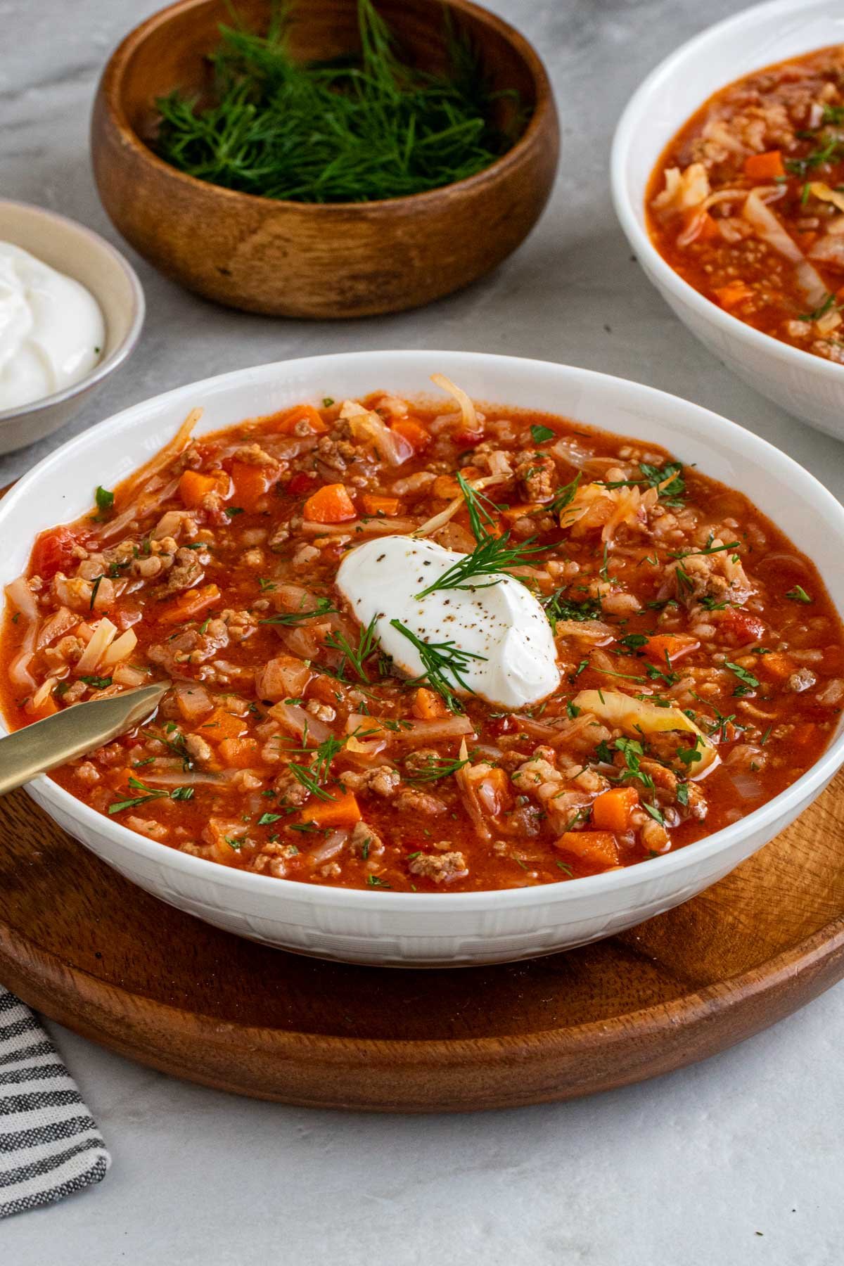 Close up of cabbage soup recipe with sour cream and dill on a wood serving platter.