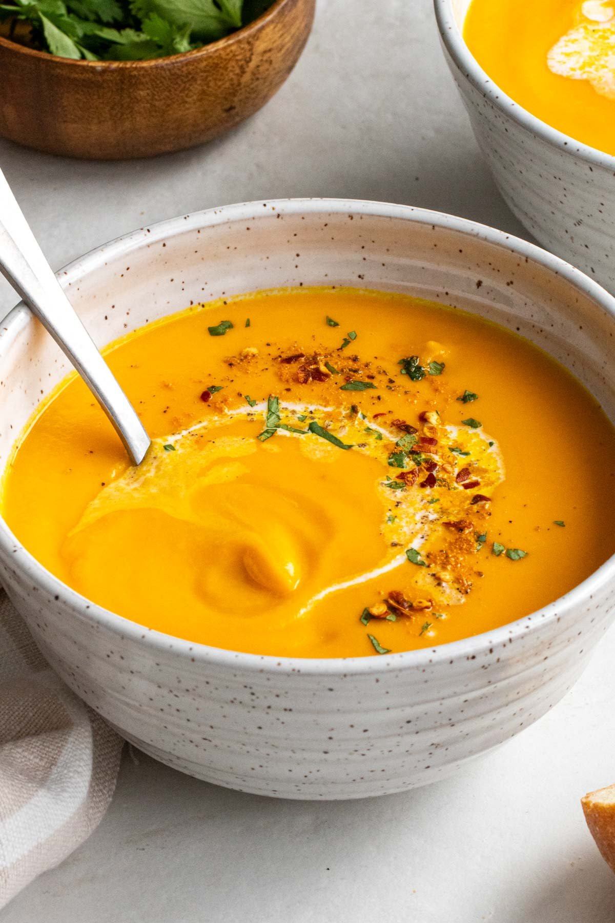 Close up of bowl of ginger carrot soup in a speckled beige bowl with an antique silver spoon.