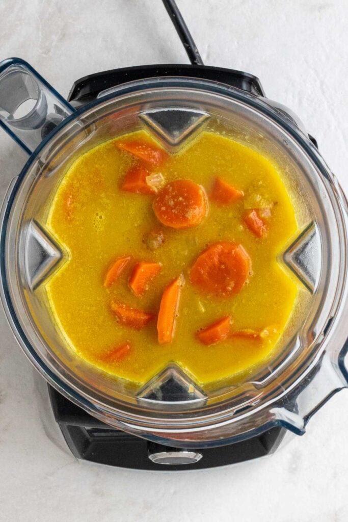 Blender with cooked carrots and ginger in coconut milk broth.