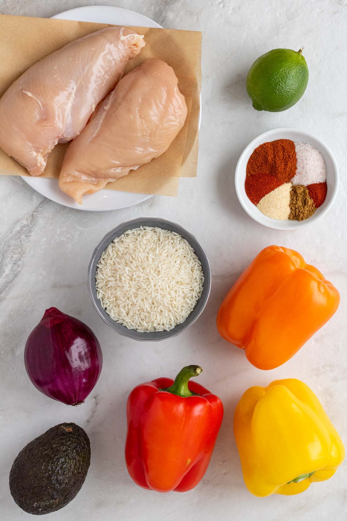 Ingredients for meal prep chicken fajita bowls: chicken breasts, white rice, bell peppers, red onion, fajita seasoning, avocados, cilantro, and limes.