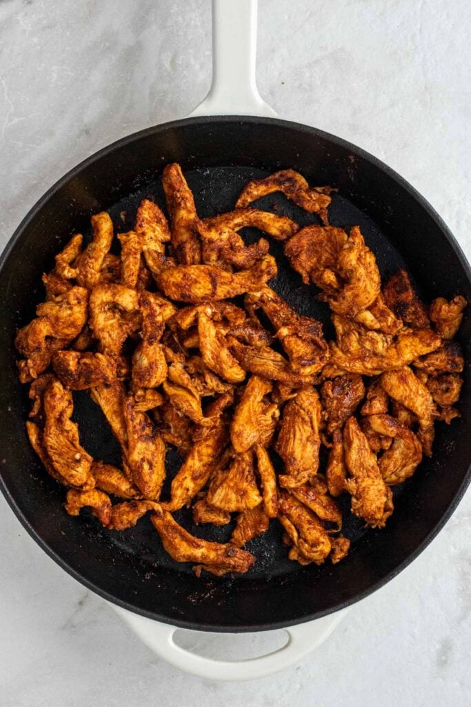 Cast-iron skillet with cooked fajita chicken strips. 