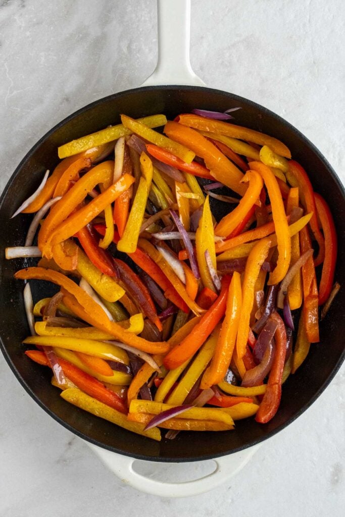 Cast-iron skillet with sautéed sliced bell pepper slices.