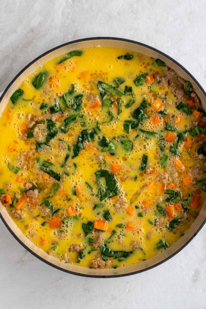 Skillet with onion, sausage, sweet potatoes, and spinach covered in an egg mixture.