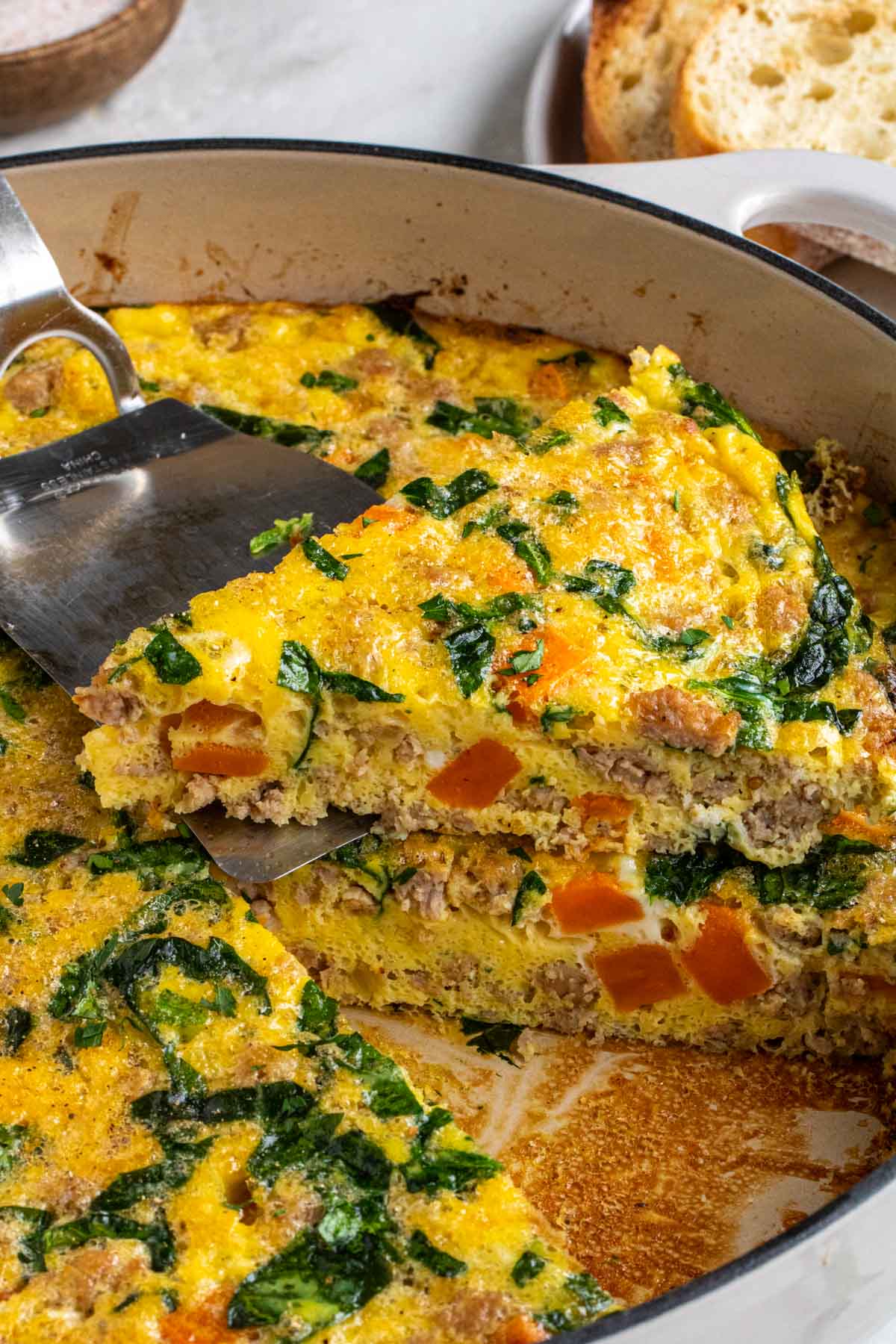 Close up of a skilelt with sausage and sweet potato frittata with a slice on a spatula on top.