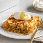 Slice of almond croissant baked oats on a white plate with Greek yogurt and maple syrup on top with a gold fork.