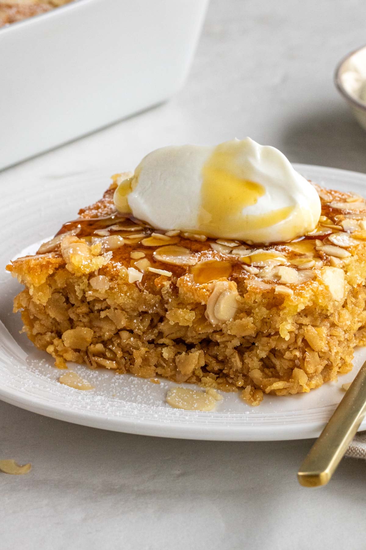 Close up of a piece of baked oatmeal with almond croissant frangipane on the top with vanilla yogurt and powdered sugar.