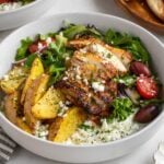 Close up of two Greek potato chicken tzatziki bowls with a side of pita bread and fresh mint on a white background.