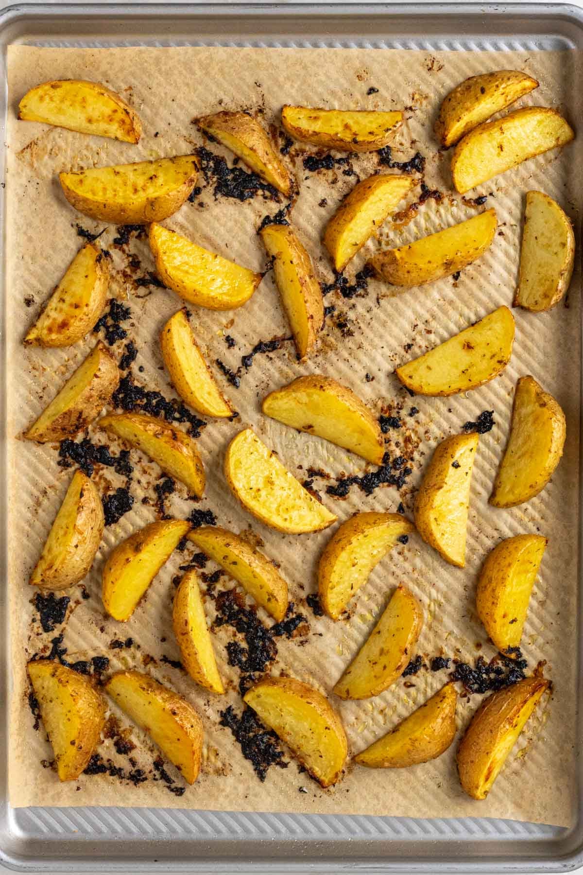 Sheet pan with parchment paper with roasted lemon potato wedges.