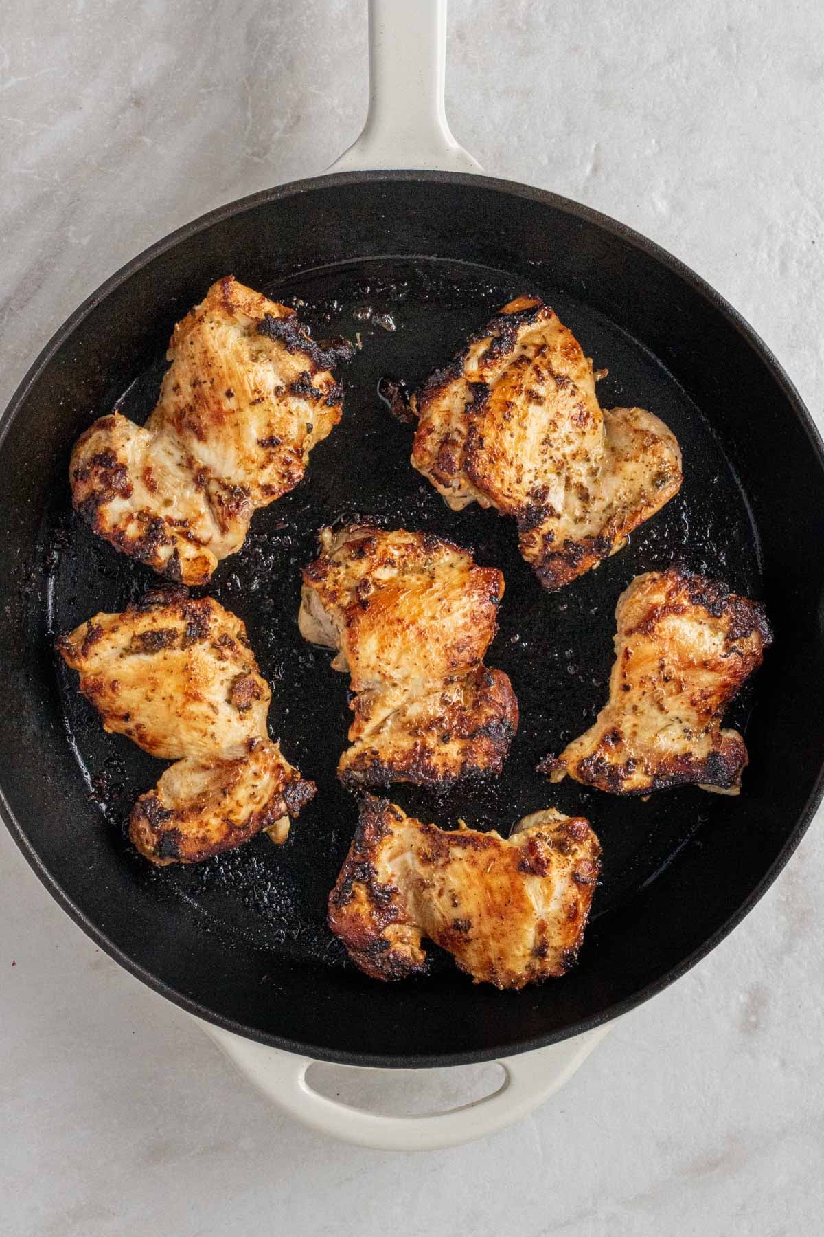Cast iron skillet with seared Greek chicken thighs.