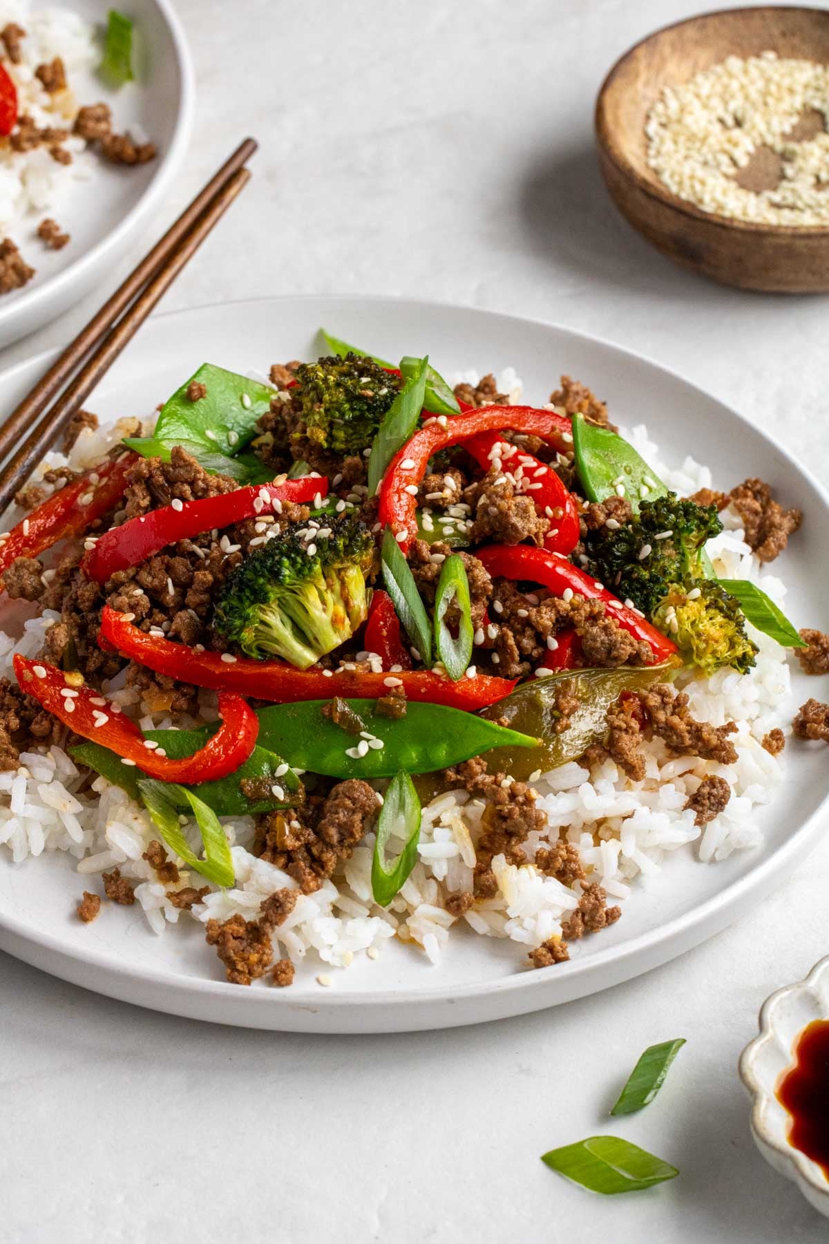 Close up of a white plate with white rice and ground beef stir fry on a white background.