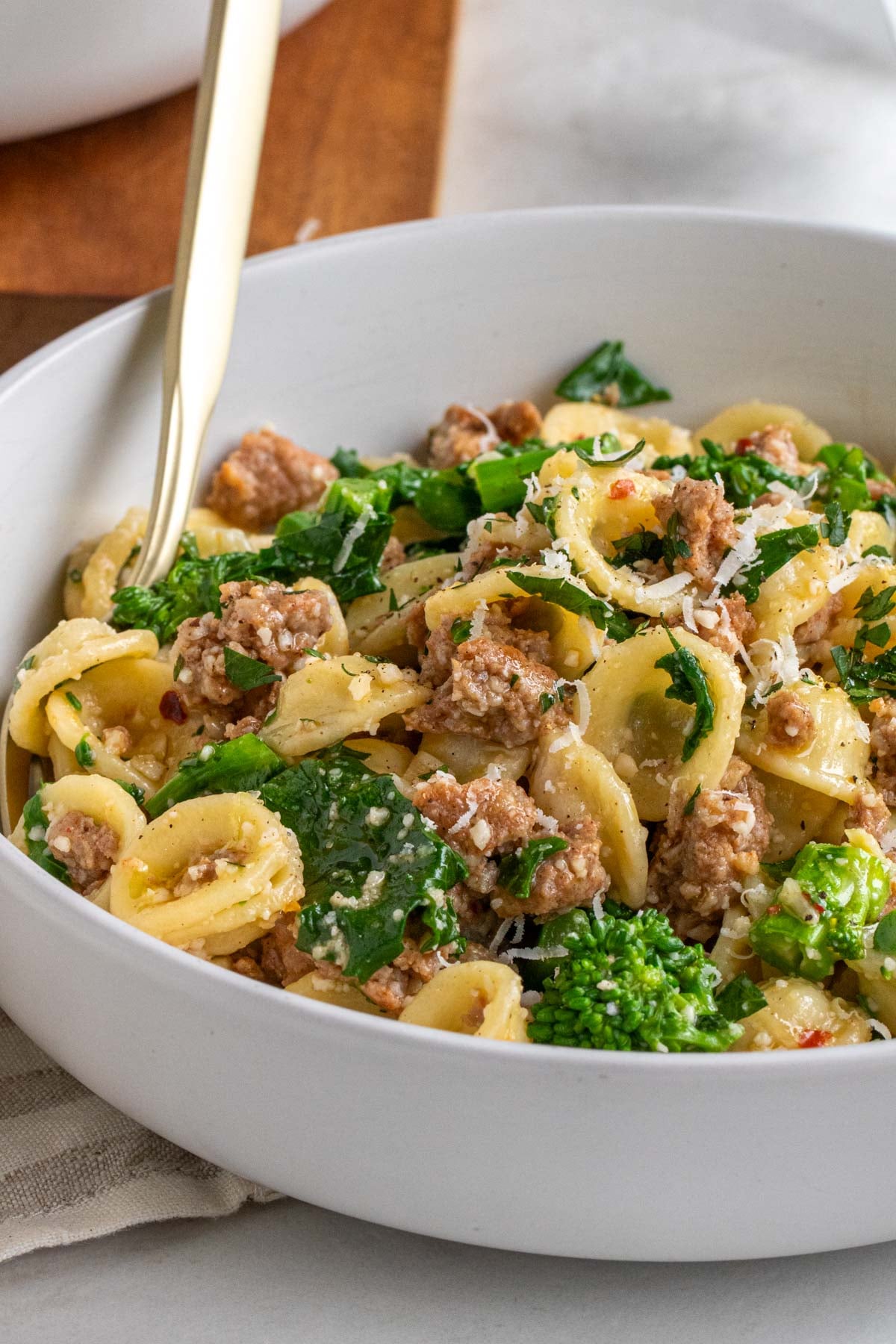 Close up of rapini and sausage pasta in a bowl with a gold fork.