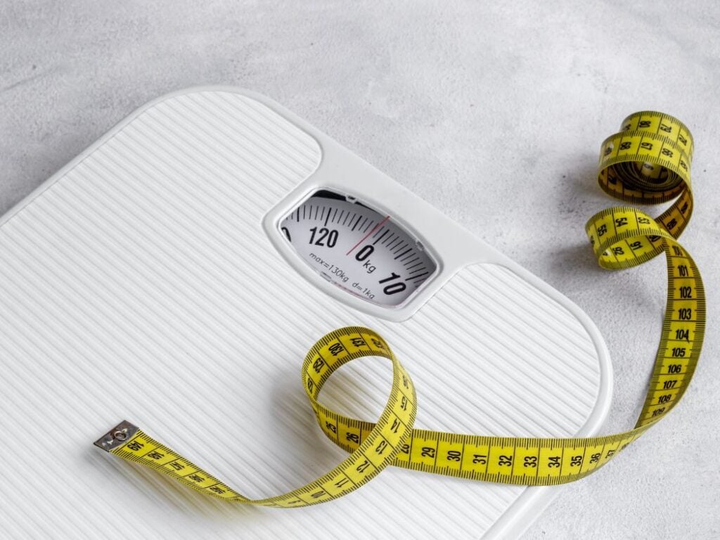 White body weight scale with a yellow sewing measuring tape on a white background.