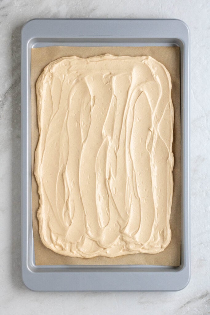 Parchment lined baking sheet with peanut butter yogurt mixture spread evenly across it.