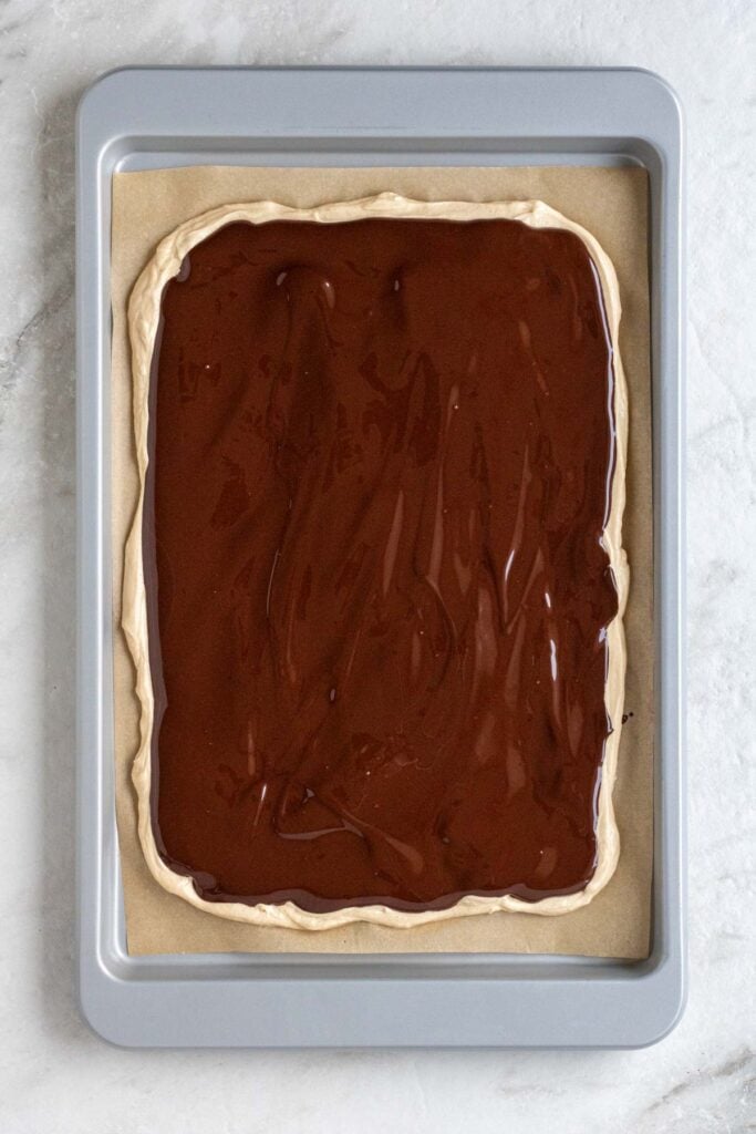 Parchment lined baking sheet with frozen peanut butter yogurt mixture with melted dark chocolate on top.