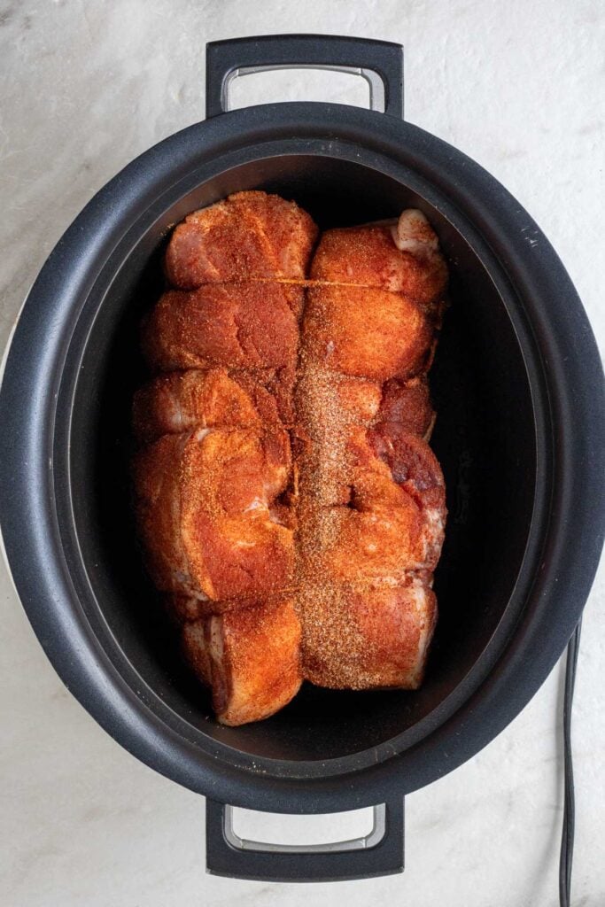 Raw pork shoulder covered in spices in a slow cooker.