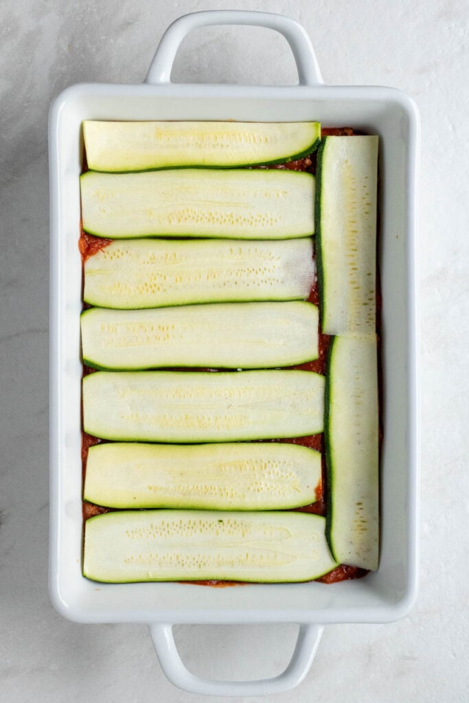 White baking dish with meat sauce covered in zucchini slices.