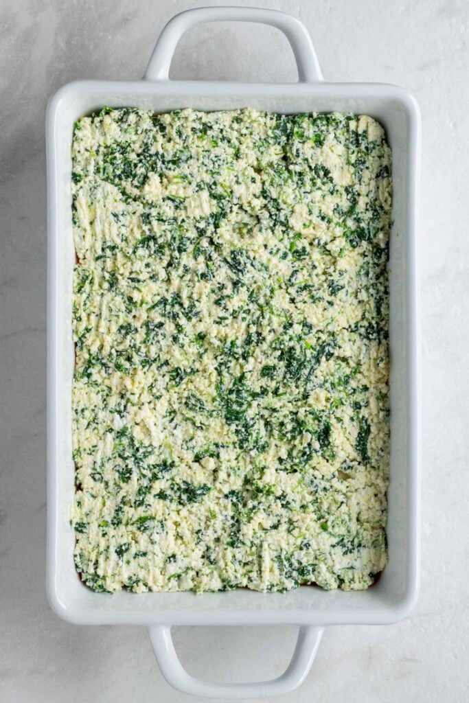 White baking dish with zucchini slices covered in spinach ricotta mixture.