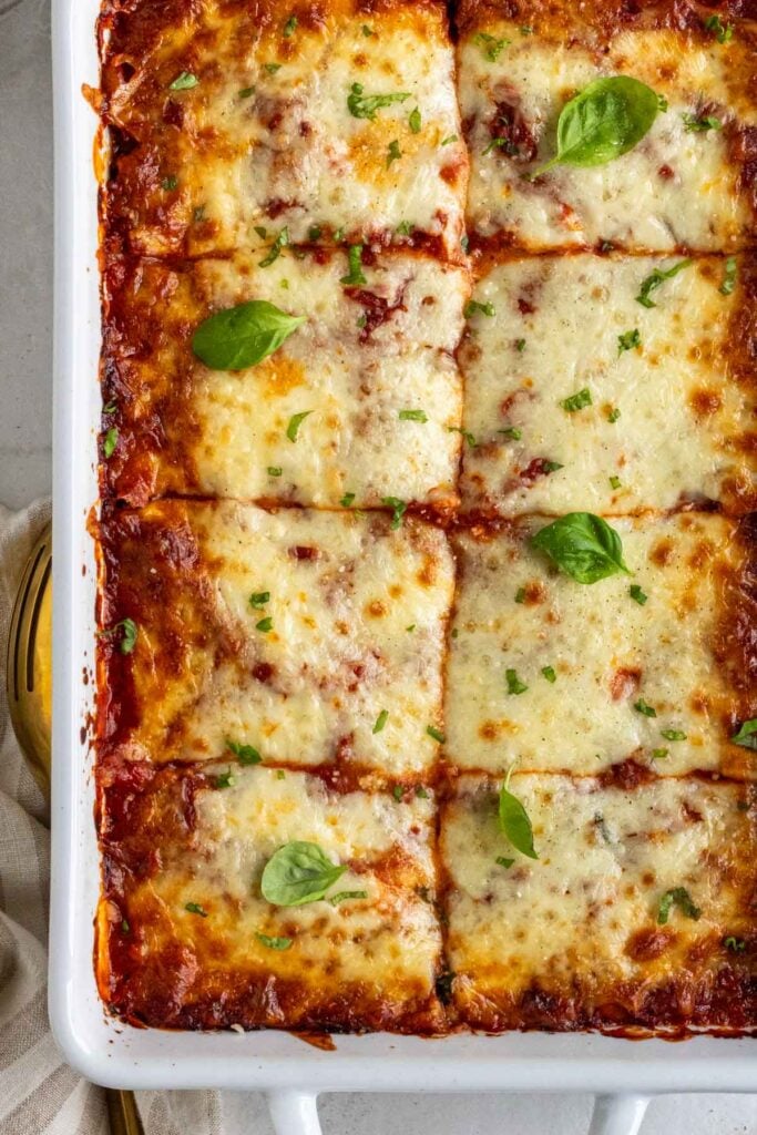 Large white baking dish with zucchini lasagna with fresh basil and freshly grated parmesan on top.