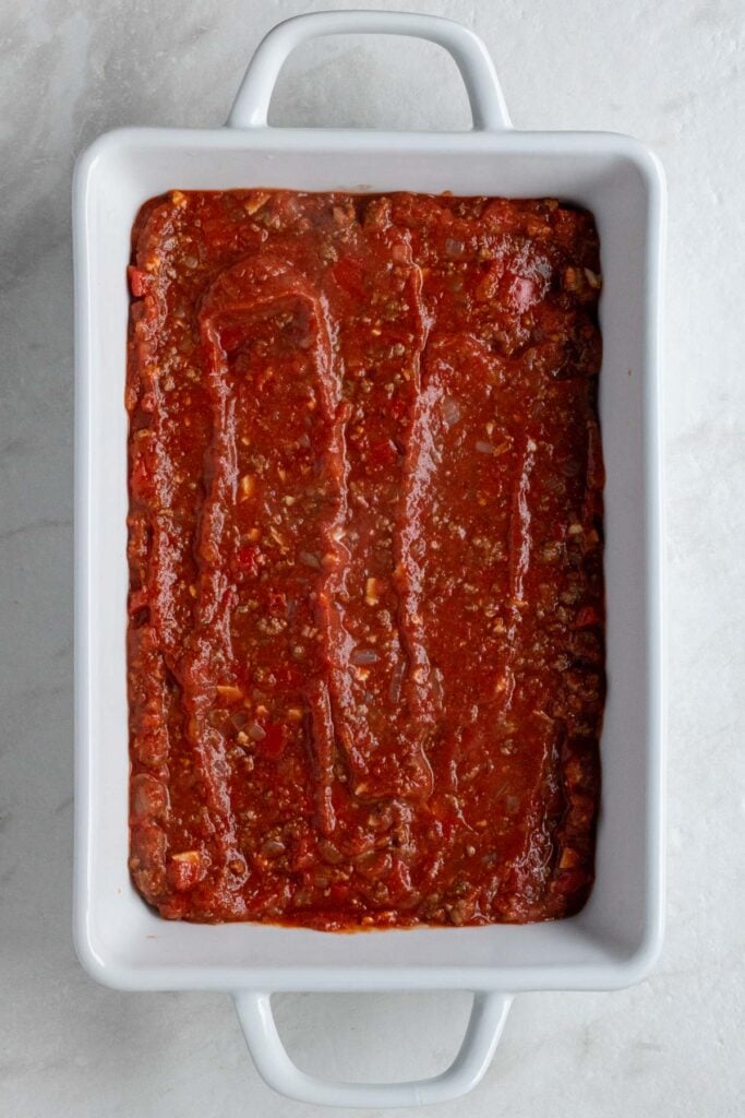 White baking dish with zucchini slices covered in meat sauce.