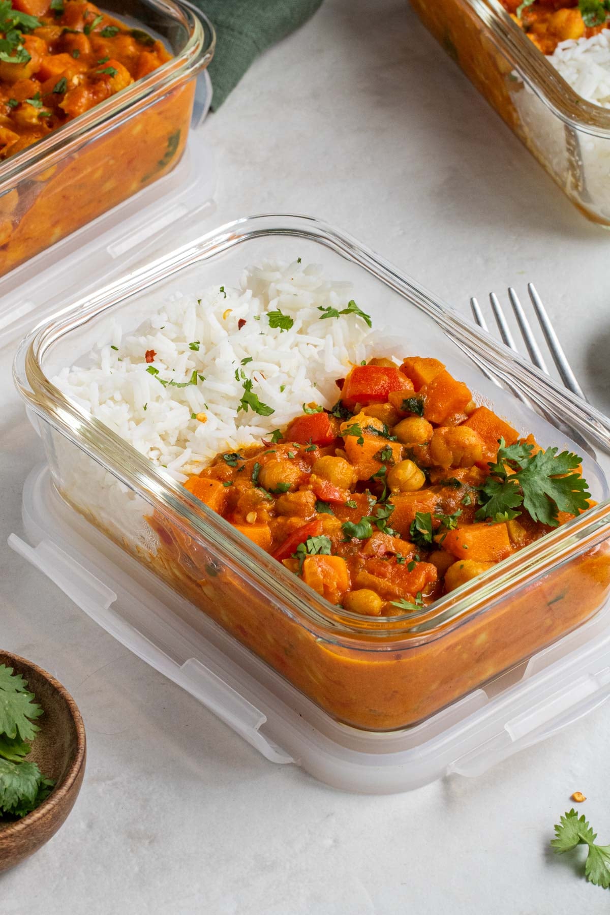 Close up of chickpea curry in a glass meal prep container with a fork and chopped cilantro on the side.