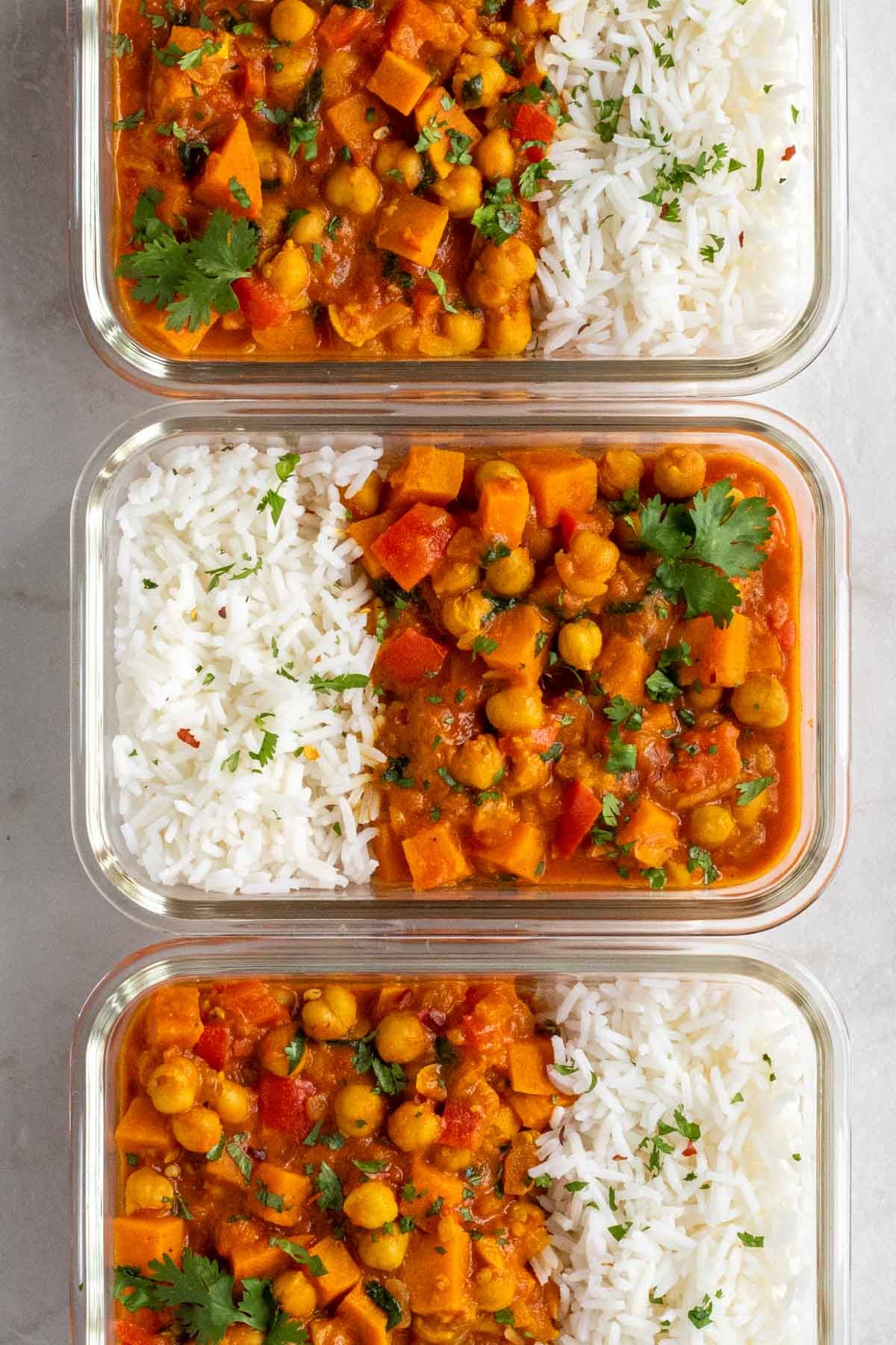 Close up of three lined up meal prep bowls with chickpea curry and white rice.