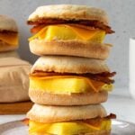 Three meal prep breakfast sandwiches stacked on a plate with a breakfast egg sandwich wrapped in parchment paper in the background.