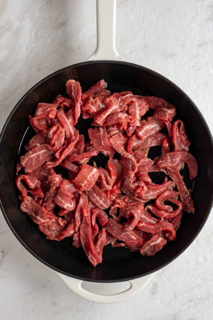 Cast iron skillet with raw sliced flank steak.