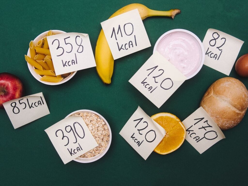 Different foods with a post it note label of the number of calories they contain on a dark green background.