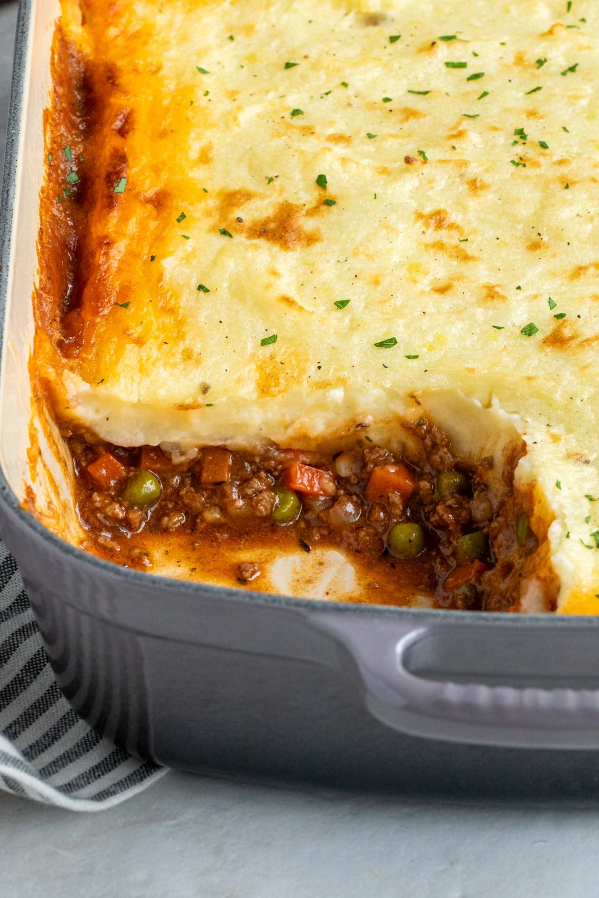 Close up of shepherd's pie in grey baking dish with a slice missing.