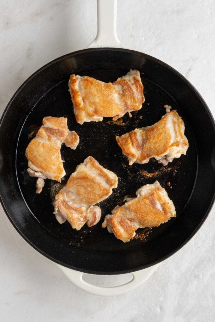 Cast-iron skillet with seared boneless chicken thighs.