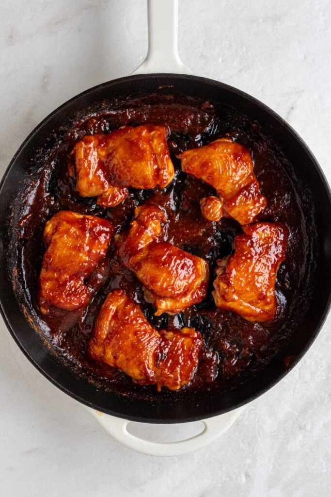Cast-iron skillet with seared chicken thighs covered in gochujang sauce.