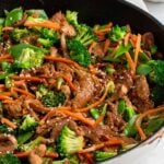 Large pan of ginger pork stir fry with broccoli, carrots, and snow peas with sesame seeds sprinkled on top.