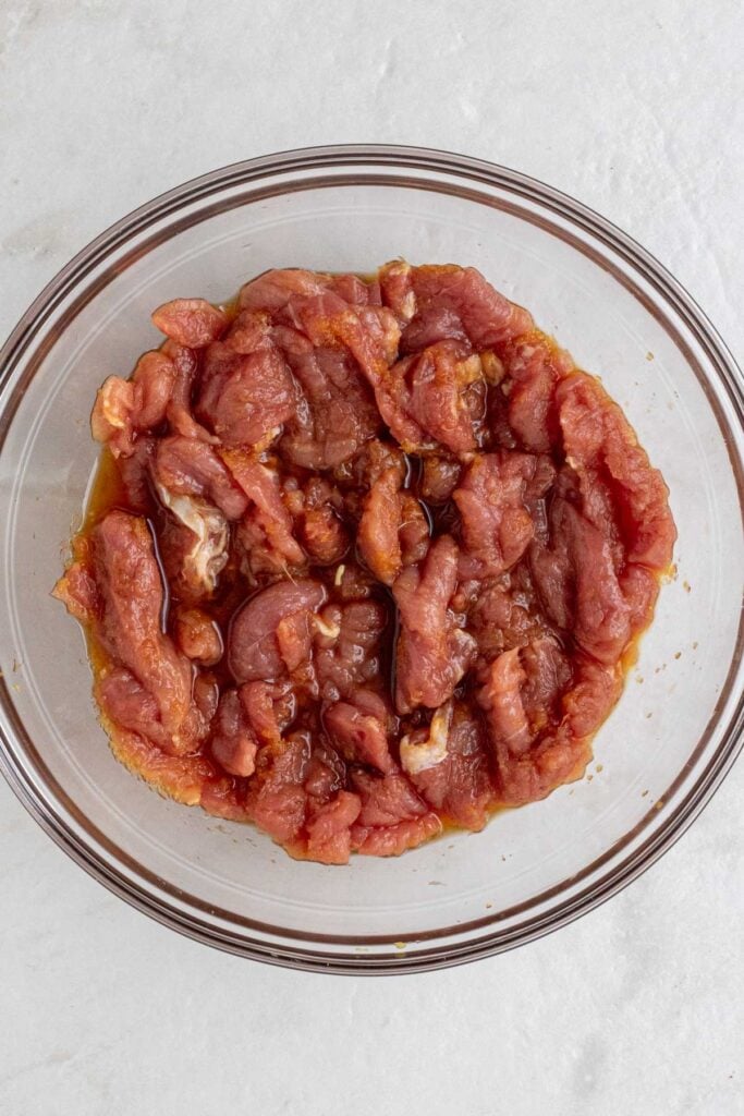 Glass bowl of sliced pork tenderloin in marinade.