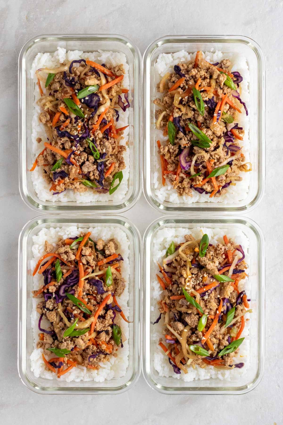 Four meal prep egg roll in a bowl with white rice in glass containers on a white background.