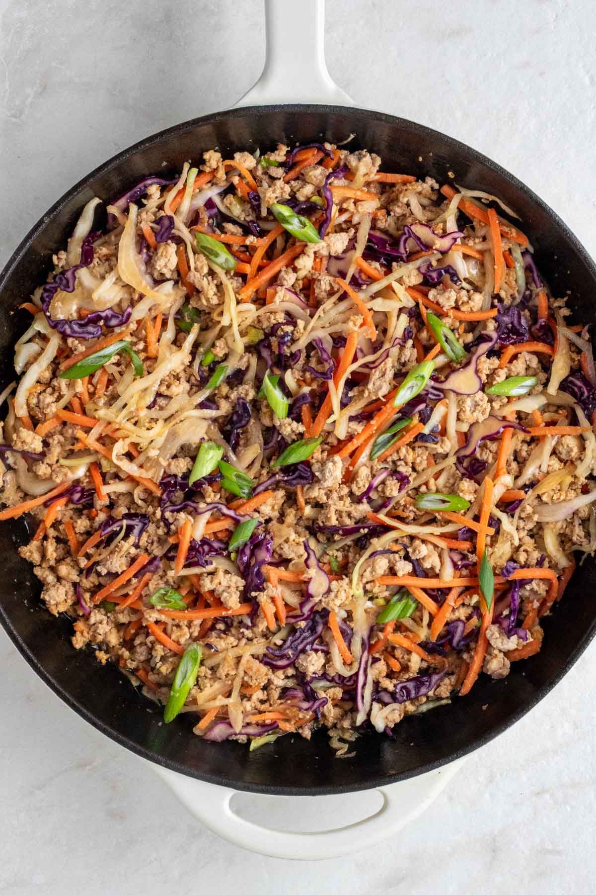 Large pan of cooked egg roll in a bowl mixture with sliced green onion and sesame seeds on top on a white background.