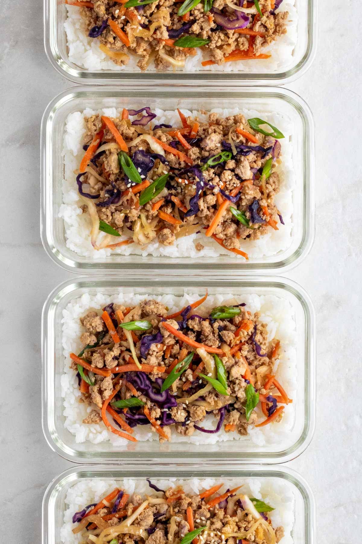 Line of glass meal prep containers filled with white rice and pork egg roll in a bowl mixture.