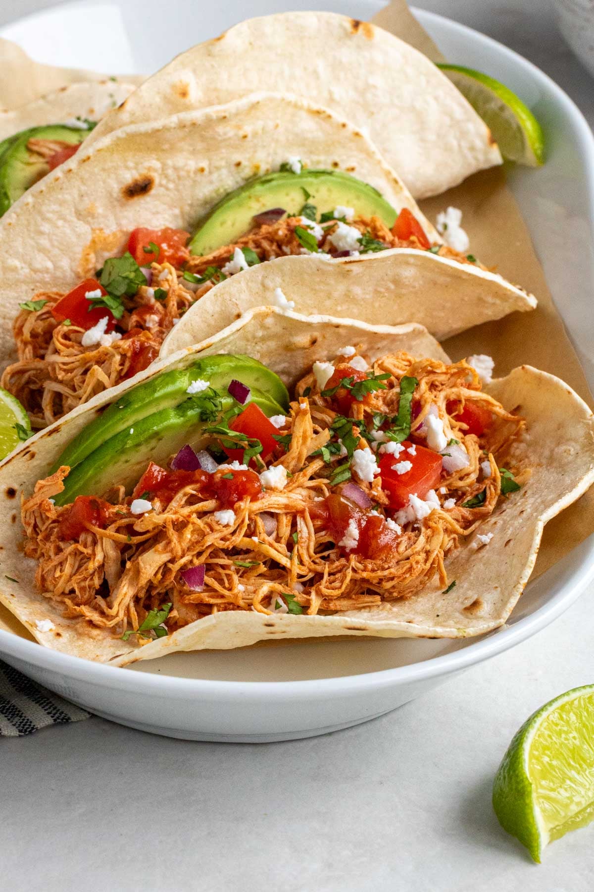 Plate of crock pot chicken tacos on parchment paper with a tea towel on the side.