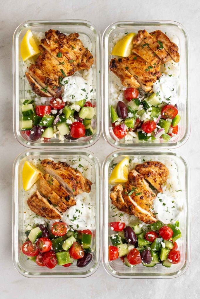 Four glass containers or Greek chicken meal prep bowls on a white background.